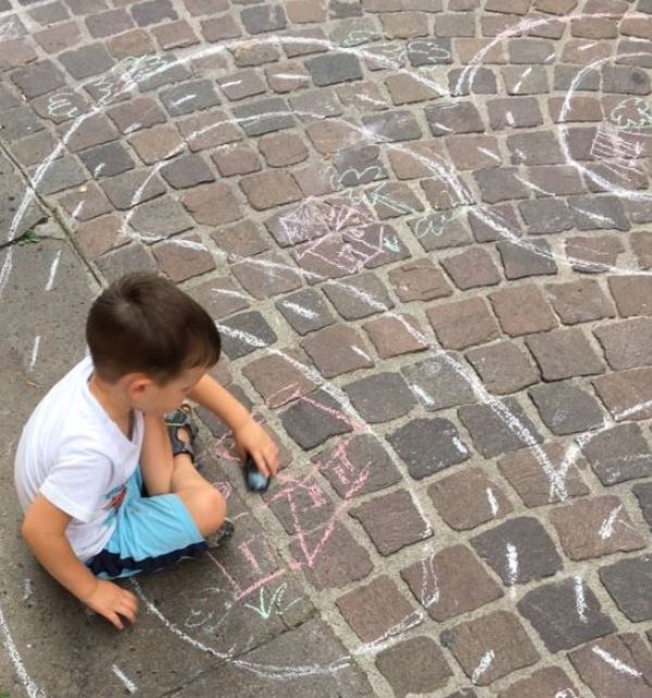 Un bambino disegna con i gessetti sul pavimento e gioca con il modellino di una macchina
